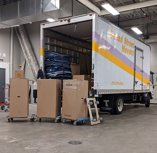 A truck from Broad Street Movers parked inside a warehouse during a local commercial move with several tall boxes sitting on dollies after being unloaded from the truck.